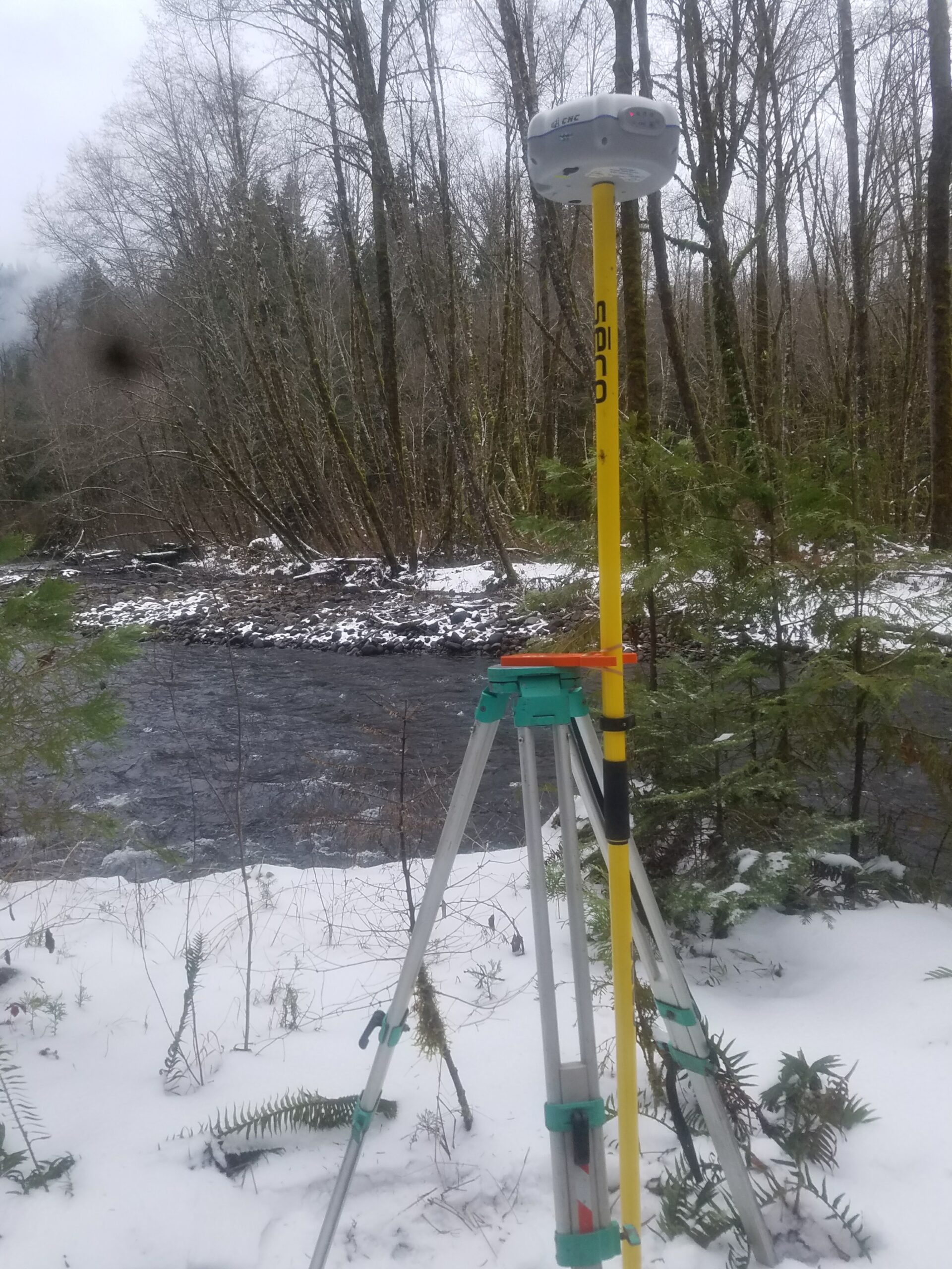 Surveying equipment set up in a snowy landscape near a river